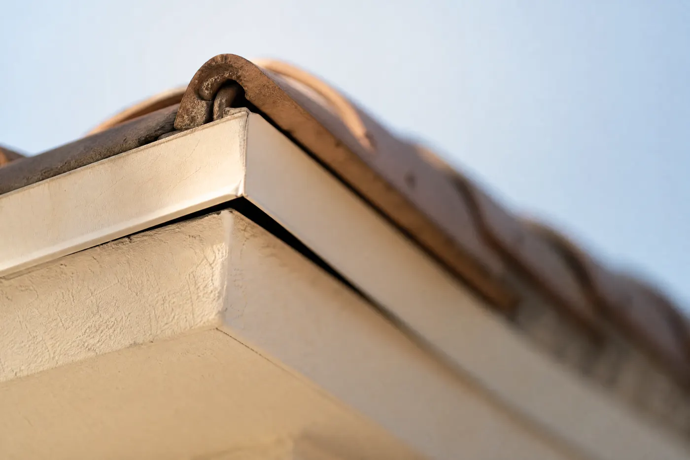 Exterior corner where a tile roof plane meets a stucco wall and the soffit dead-ends, with a dark open gap along the seam