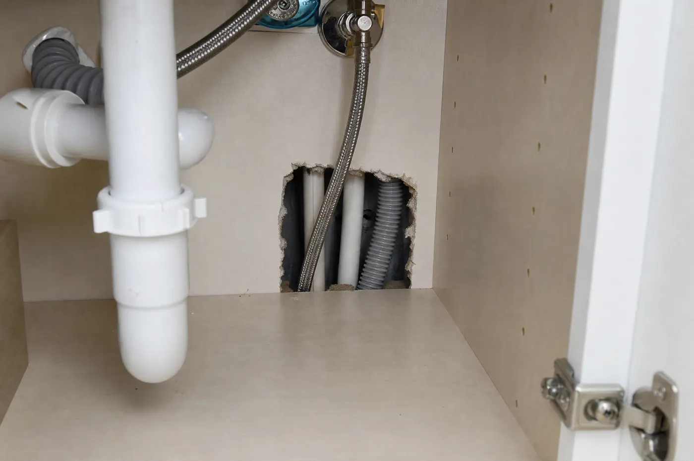 Apartment kitchen plumbing and shared wall junction with small gaps around utility lines