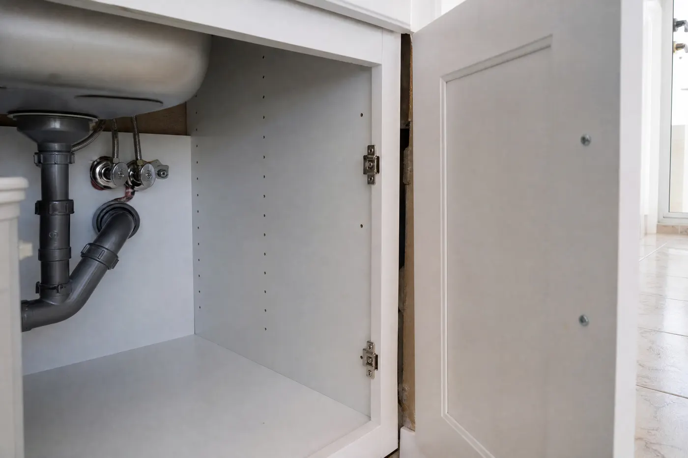 Gabinete de fregadero de condominio con tuberías entrando a una pared compartida